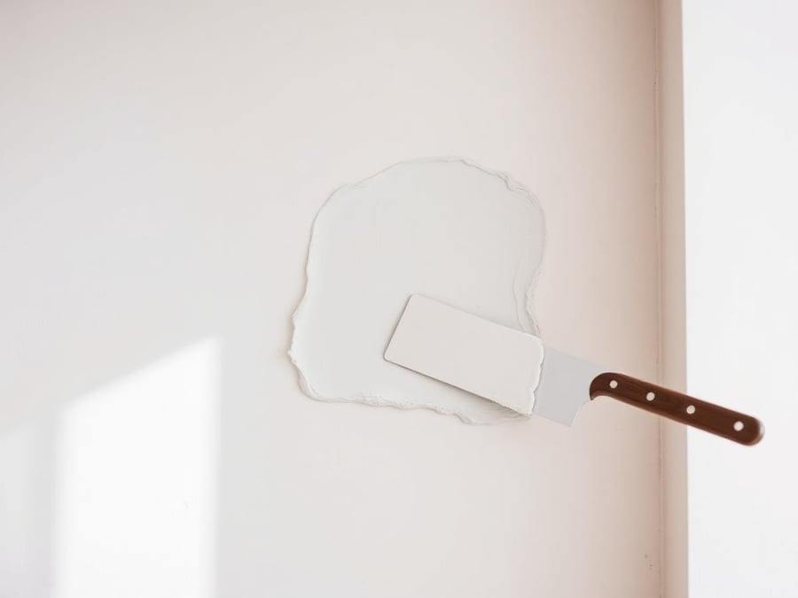 Illustrative example: a drywall patch being smoothed flat with a wide taping knife.